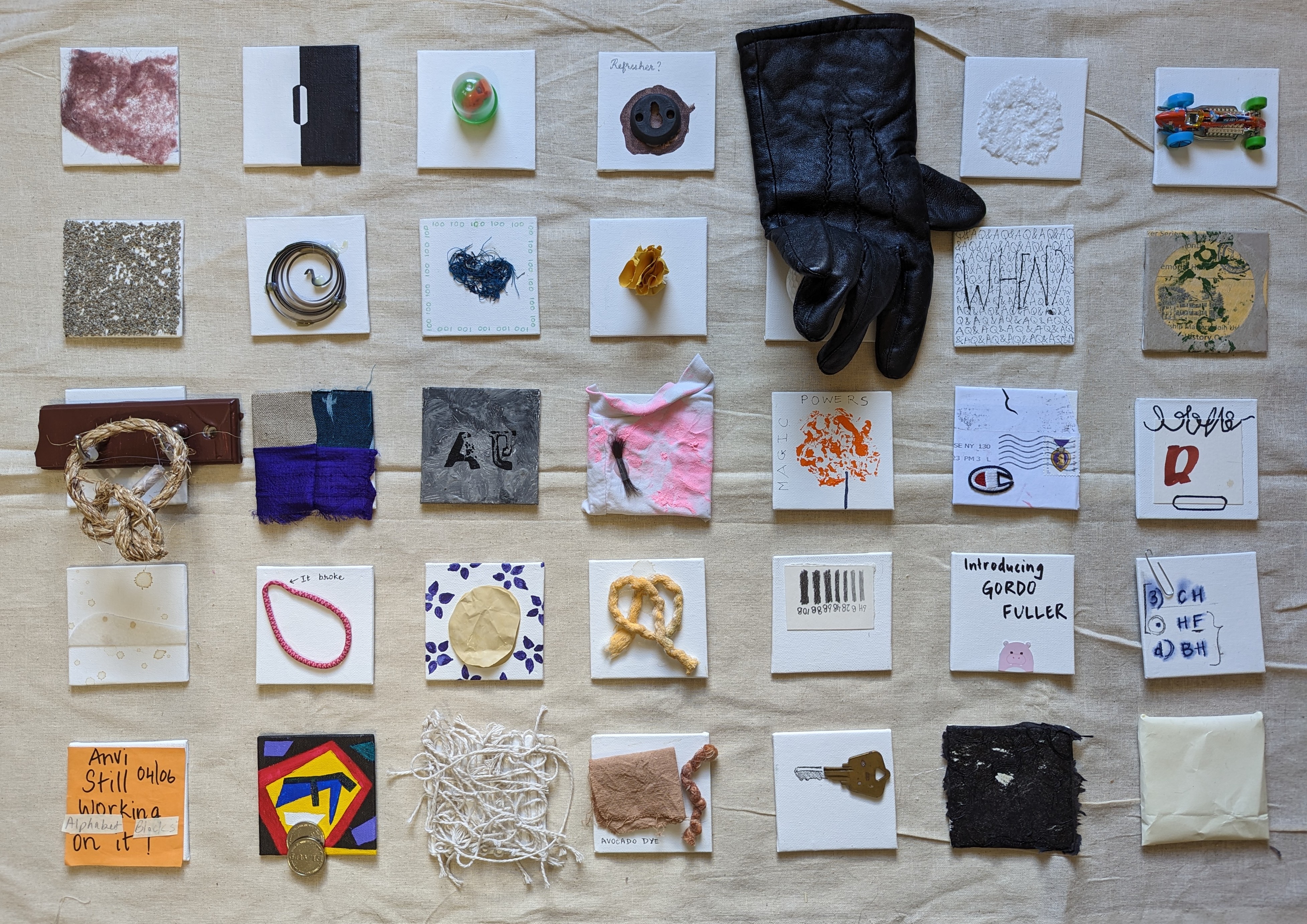 Large wall installation of approximately 35 small mixed-media assemblages on pale linen in 5 rows: rubber bouncy ball, rusted ring with 'Refresher?' label, black leather glove, toy plastic car, coiled metal spring, thread fringe with repetitive numbers, postmarked Champion envelope, pig drawing labeled 'Introducing GORDO FULLER', brass key, and charred paper scraps.
