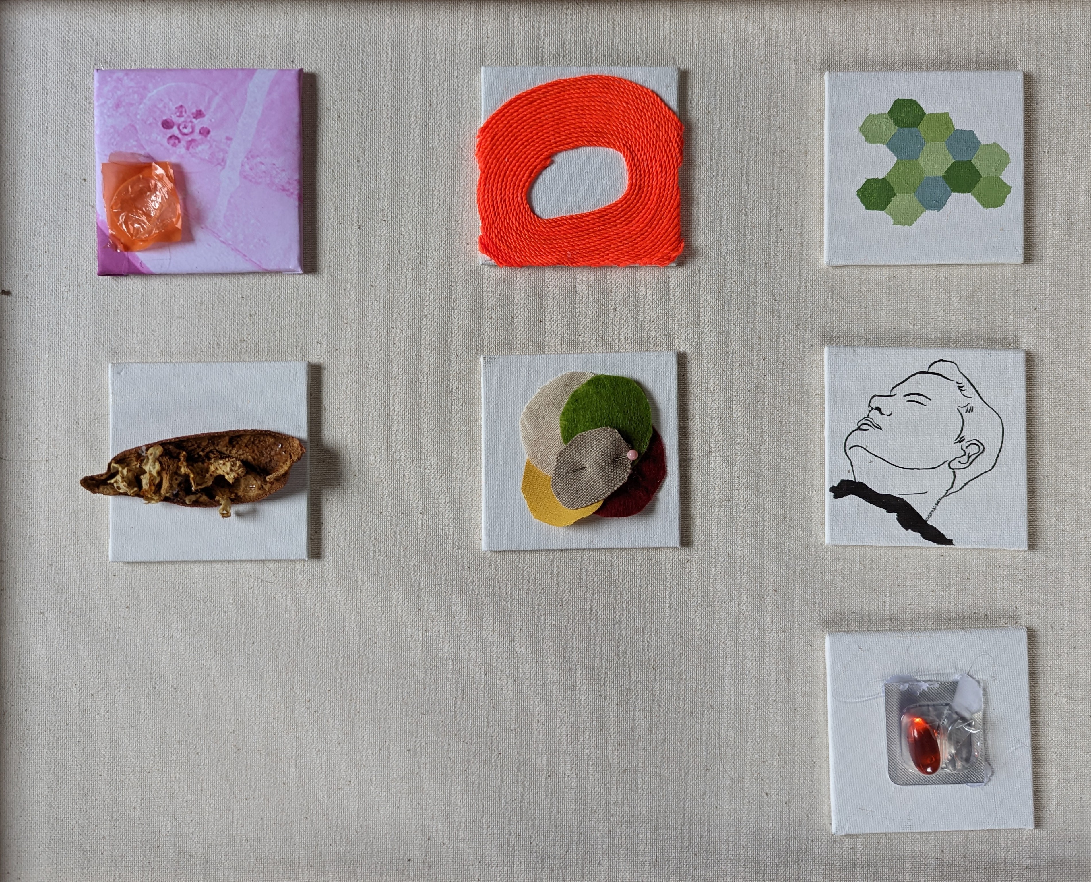 Grid of 7 small assemblages on linen: painted canvas with wrapped orange candy, densely stitched orange embroidery floss forming an oval ring, painted green hexagonal mosaic pattern, single brown seed pod form, overlapping felt pieces with pink bead, ink line drawing of a reclining face, and foil blister pack with two orange capsule pills.